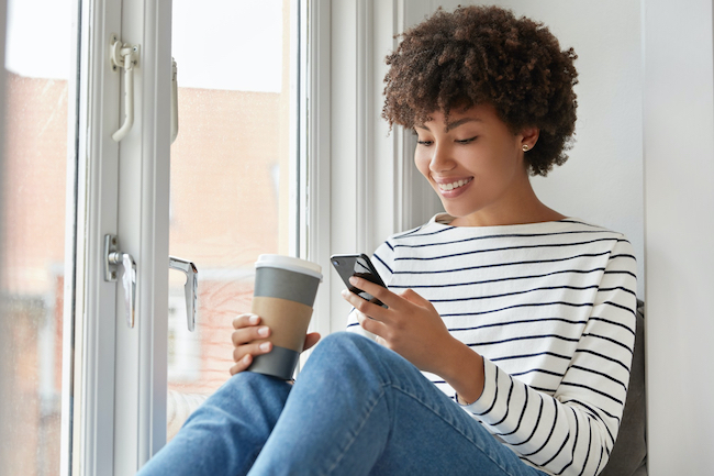 happy-dark-skinned-female-with-pleased-expression-reads-online-book-via-cell-phone-checks-email-social-networks