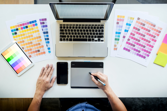 Top view of a young graphic designer working on a desktop computer and using some color swatches, top view