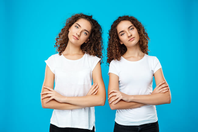 Two girls twins posing with crossed arms over blue background.